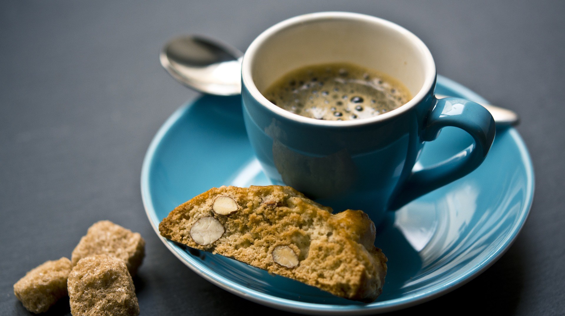 En blå kaffekopp med svart kaffe i. En skorpa ligger på kaffefatet.