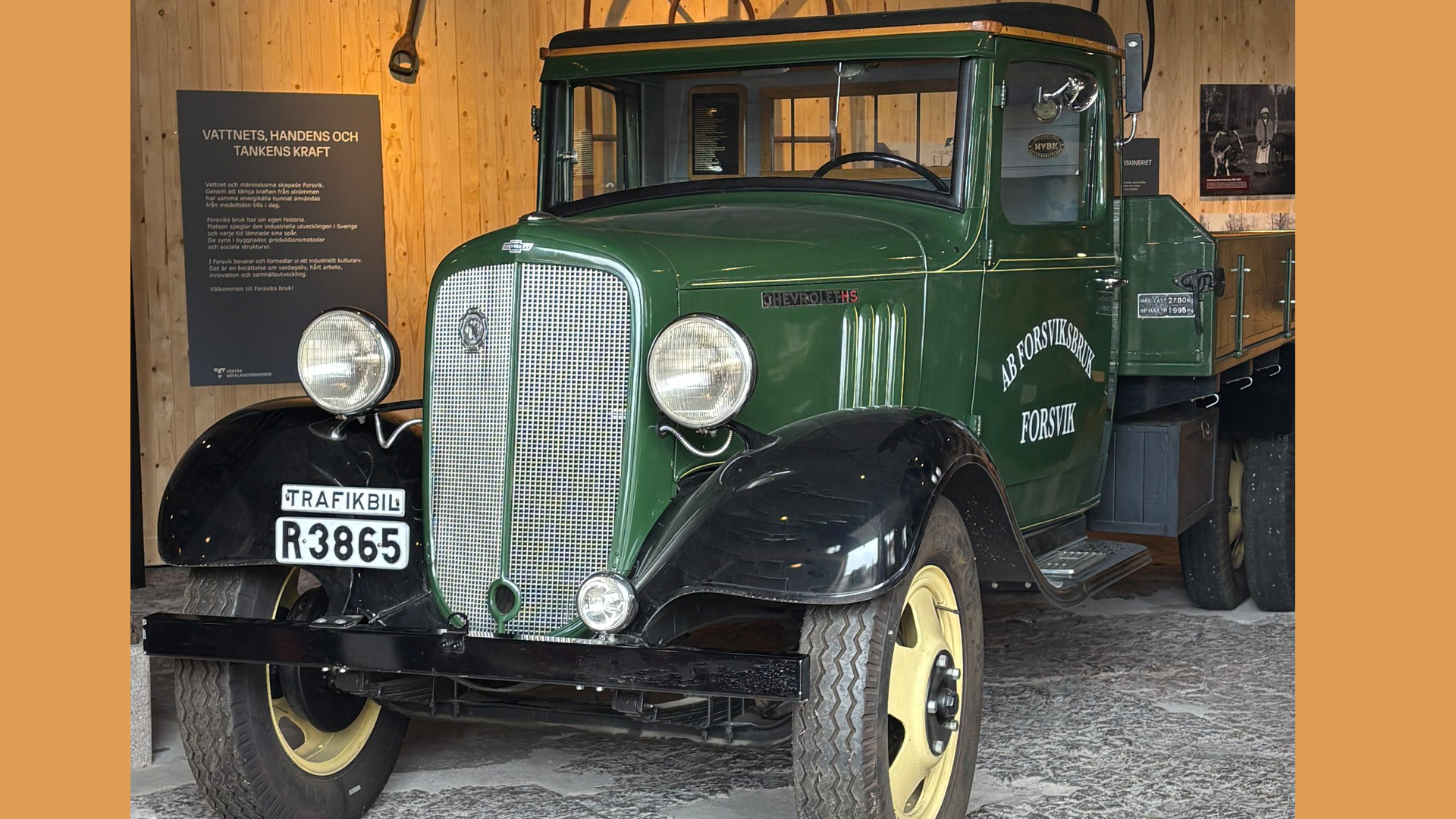 På bilden ser vi en gammal bil från 1920-talet. Den är mörkgrön. Väggarna runt har samma gula färg som senap.