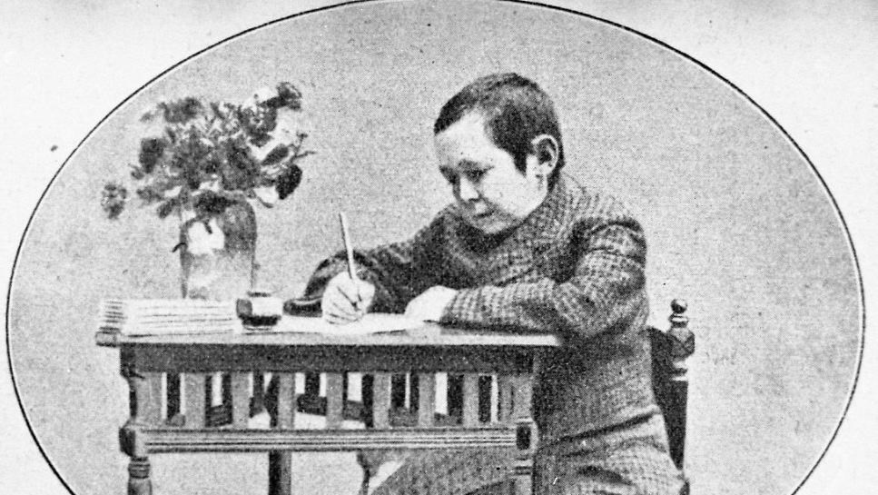 En man sitter och skriver vid ett bord med en blomvas