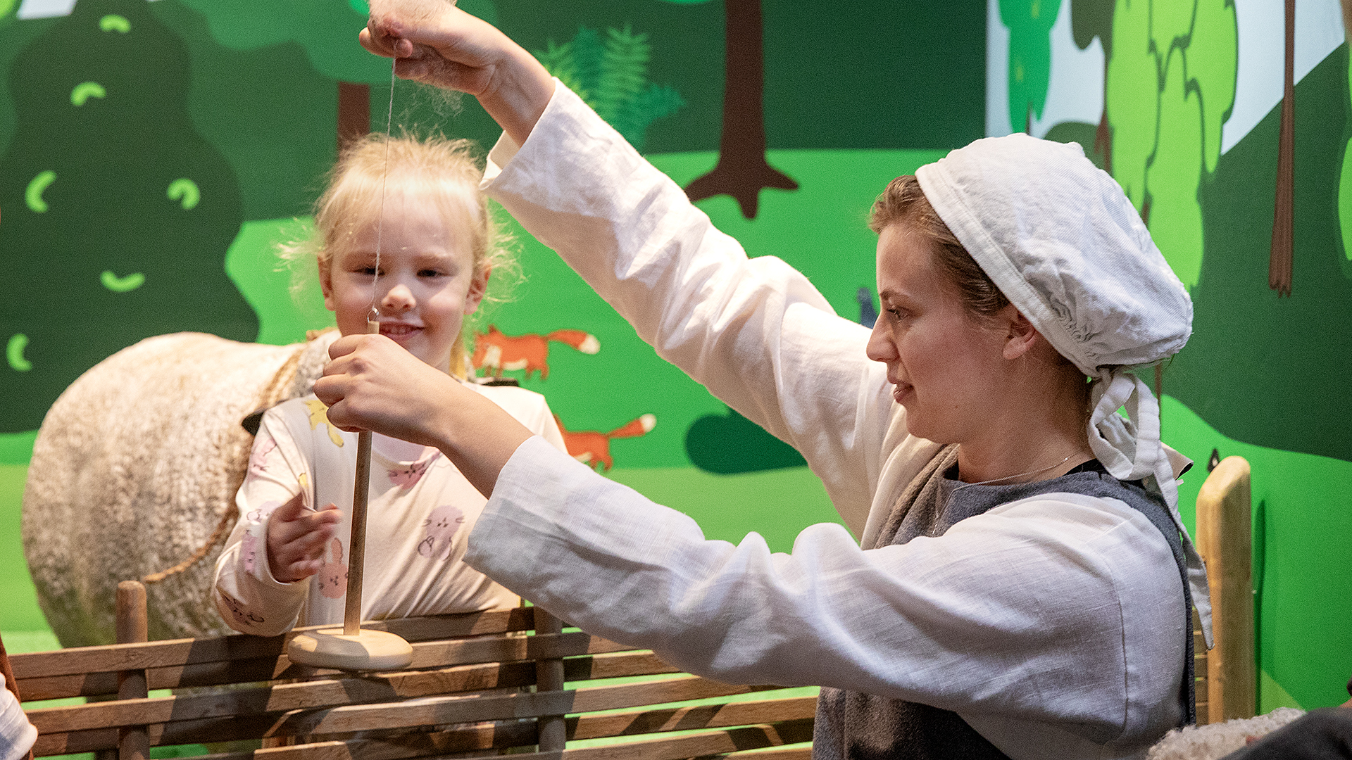 en kvinna spinnar en tråd framför ett barn